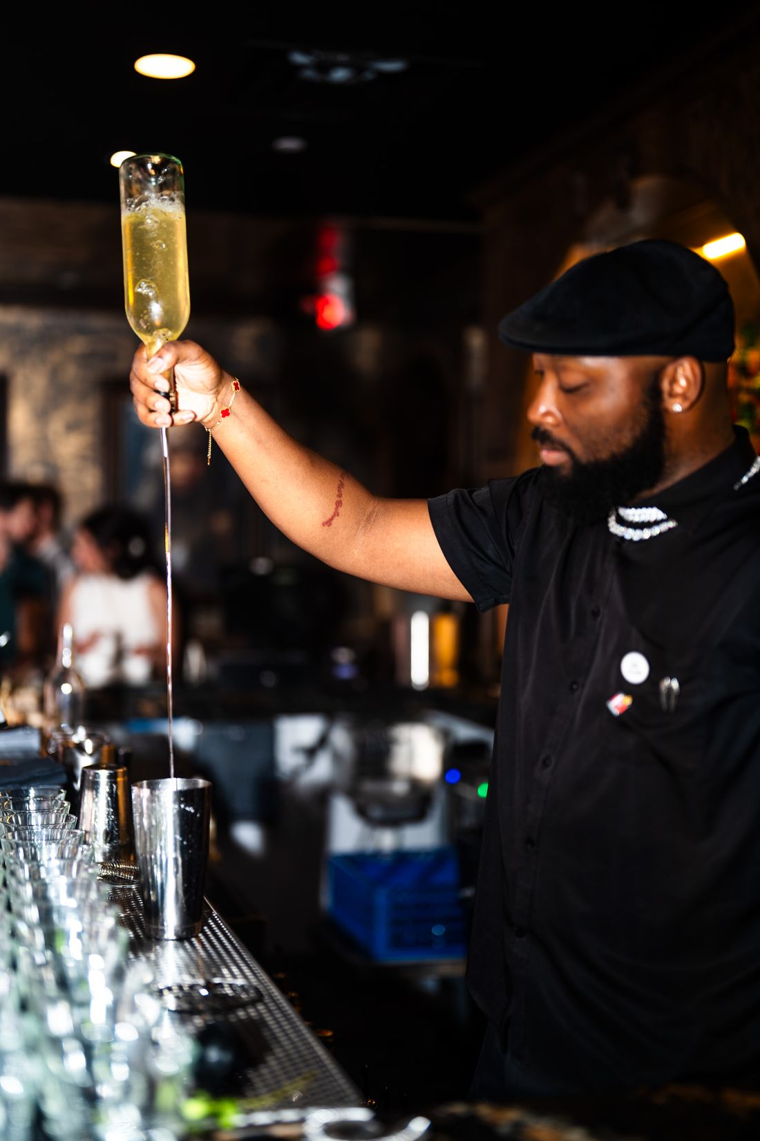 Self pouring champagne from a raised bottle into a shaker behind the bar