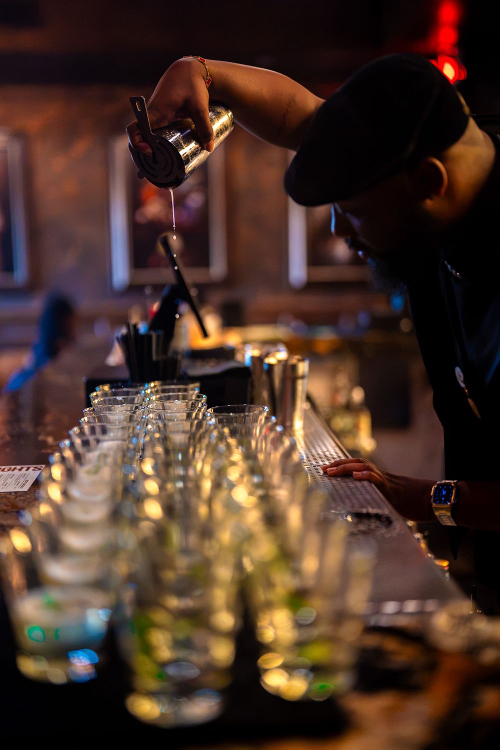 Self straining a cocktail from a shaker over a long row of glasses